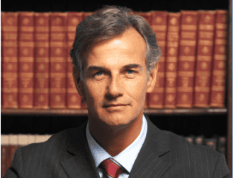 A middle-aged man in a suit and tie, embodying the professionalism of a trusted Chicago personal injury lawyer, sits in front of a bookshelf filled with leather-bound books.
