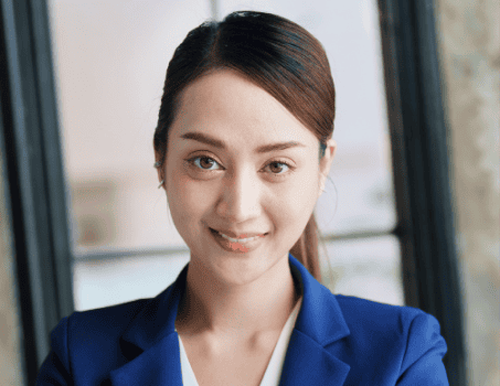A woman with long dark hair tied back, wearing a blue blazer and white top, is smiling at the camera in a well-lit indoor setting, reflecting the professionalism seen in profiles like About Lawyer Furqan.