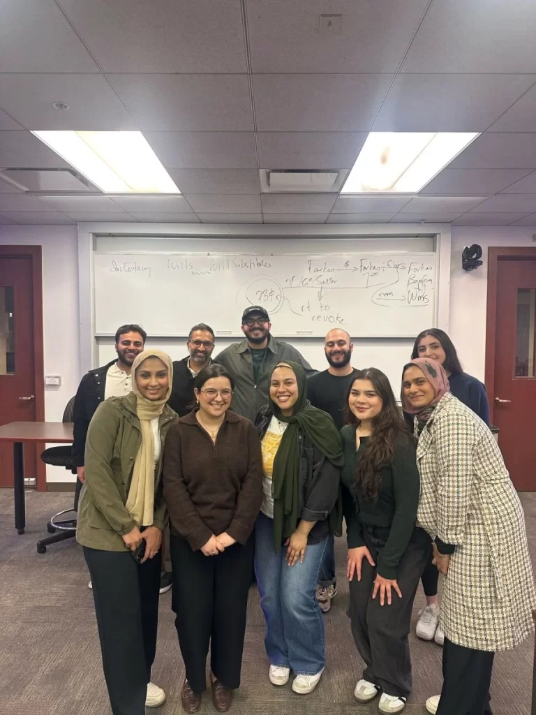 A group of ten people stand and smile in a classroom in front of a whiteboard filled with handwritten notes after Founder Furqan Mohammed speaks at webinar.