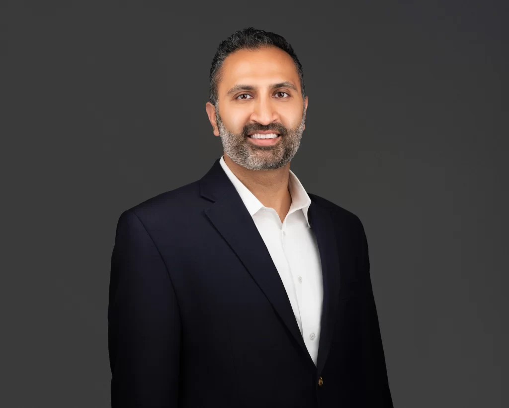 Man with short dark hair and beard, trusted Chicago personal injury lawyer, wearing a navy suit jacket and white shirt, smiling at the camera against a plain dark background.