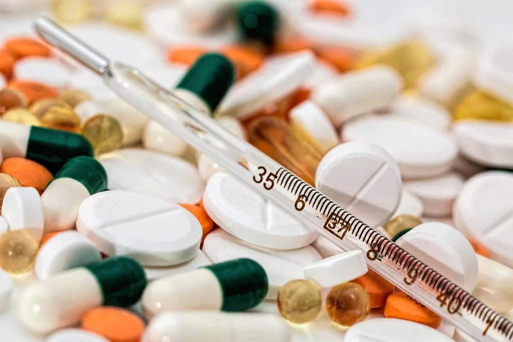 A glass thermometer rests on a pile of assorted pills, capsules, and tablets in various colors and shapes—an image highlighting risks that a Product Liability Lawyer may address.