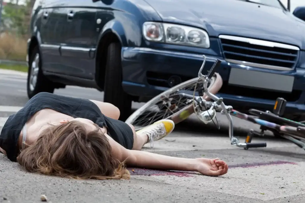 A person lies on the ground next to a fallen bicycle in front of a car, suggesting a collision—an incident where a Trusted Chicago Personal Injury Lawyer could help protect your rights.