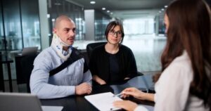 Man wearing neck brace seated with woman across desk during office meeting