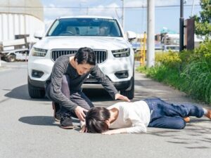 person kneeling to assist injured pedestrian lying on road in front of SUV