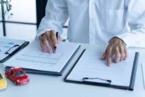 Person signing insurance forms on clipboards beside toy cars on desk