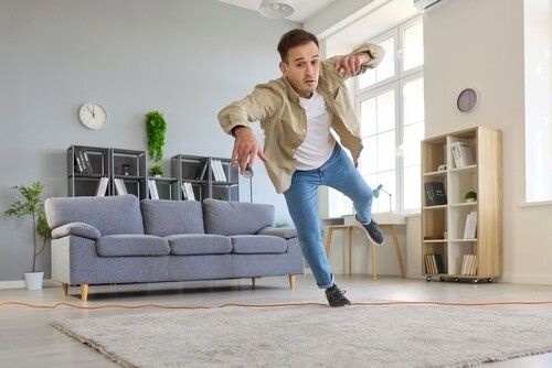 man tripping over electrical cord on living room floor losing balance
