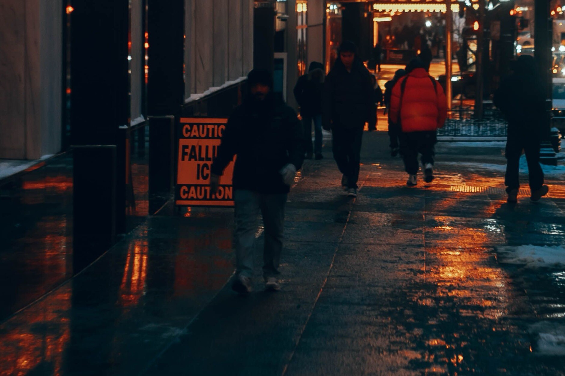 Caution Falling Ice sign on a wet Chicago sidewalk at dusk as pedestrians walk past in winter