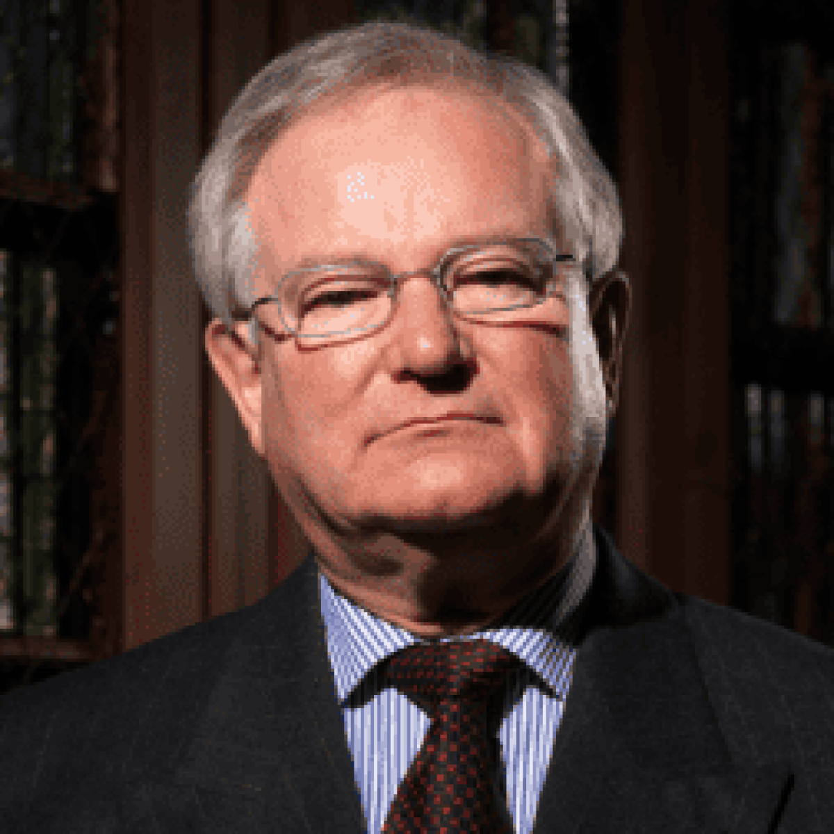 An older man with gray hair and glasses, wearing a suit and tie, stands in front of bookshelves—embodying the experience and professionalism of a Trusted Chicago Personal Injury Lawyer.