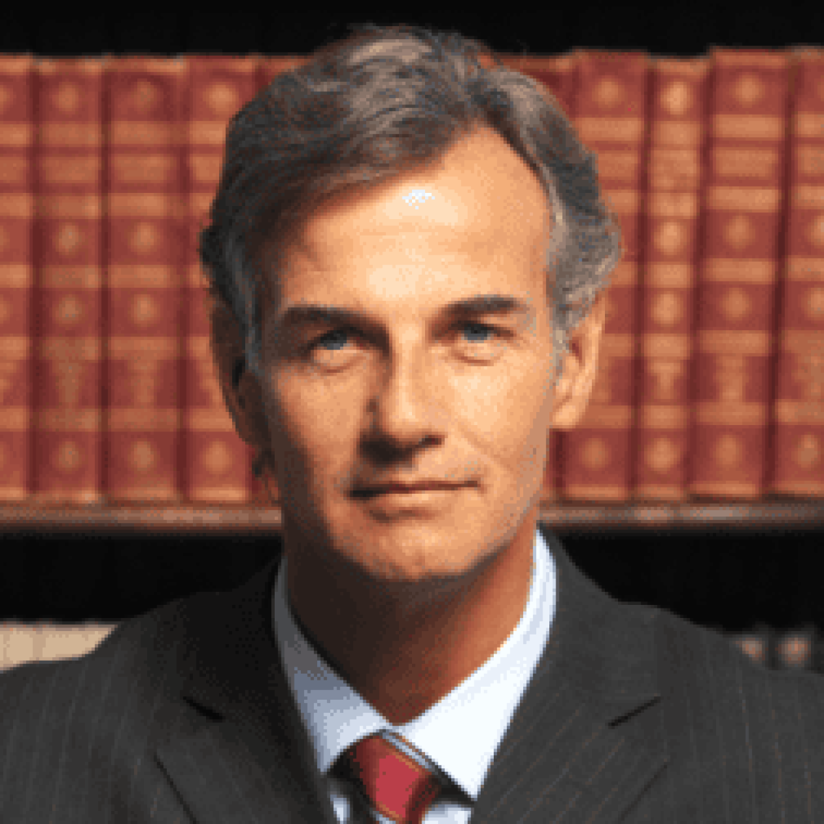 A middle-aged man in a suit and tie, embodying the professionalism of a trusted Chicago personal injury lawyer, sits in front of a bookshelf filled with leather-bound books.